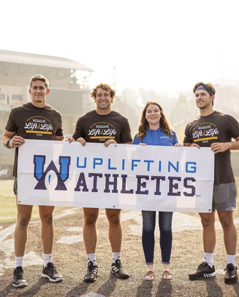 Western Michigan players standing with Uplifting Athletes' employees holding an Uplifting Athletes banner.