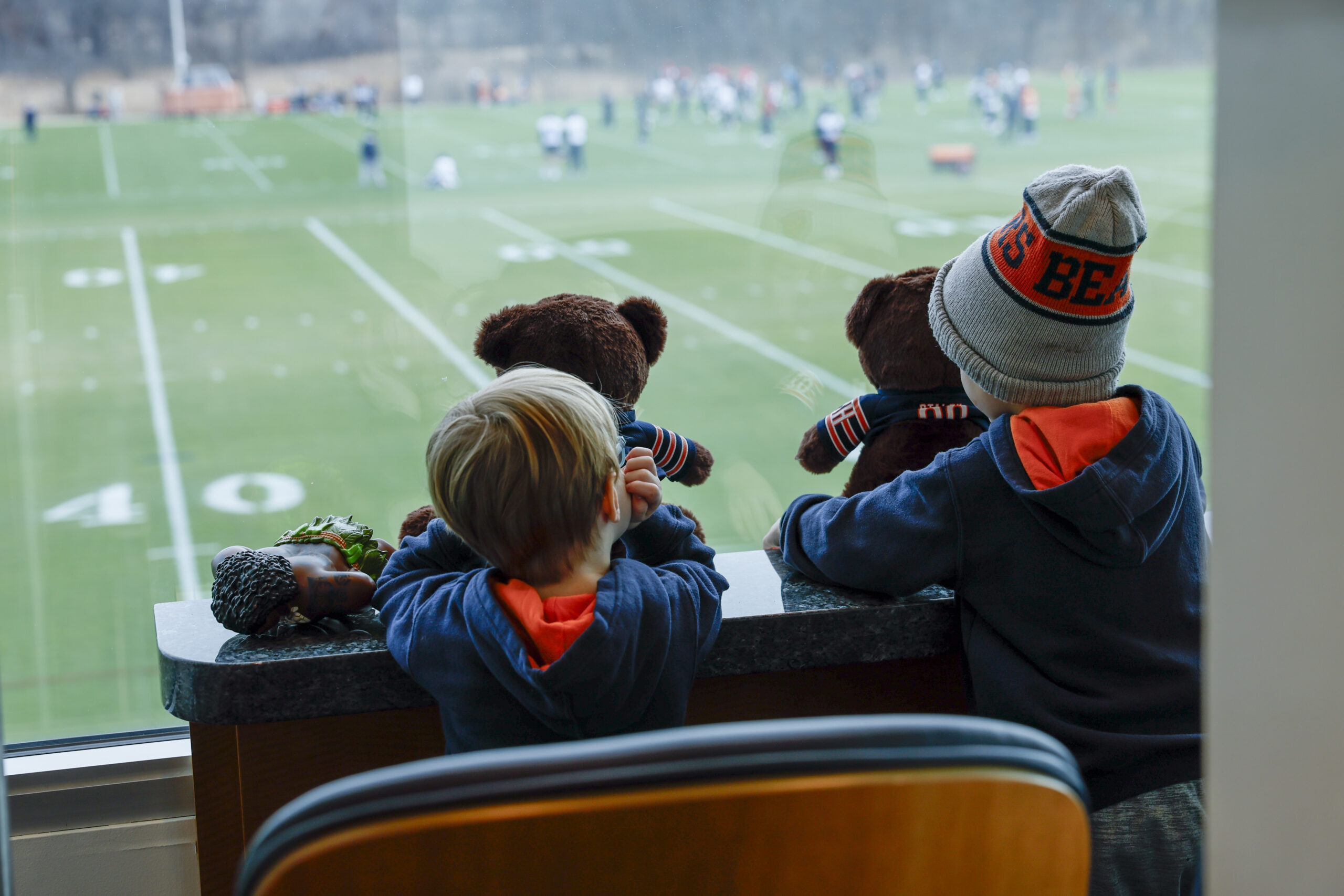 two children look out the window at the chicago bears training field while playing with teddy bears